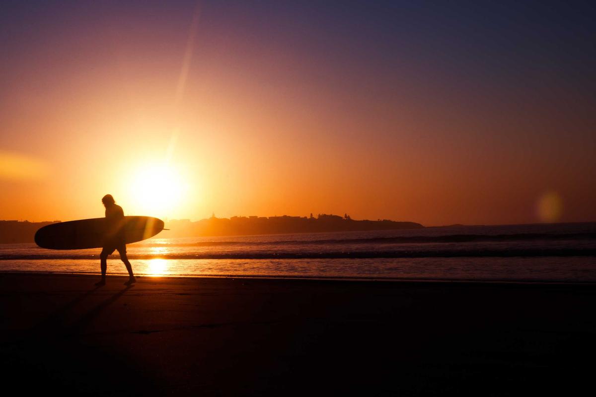 Surfer walking along the coast at sunset